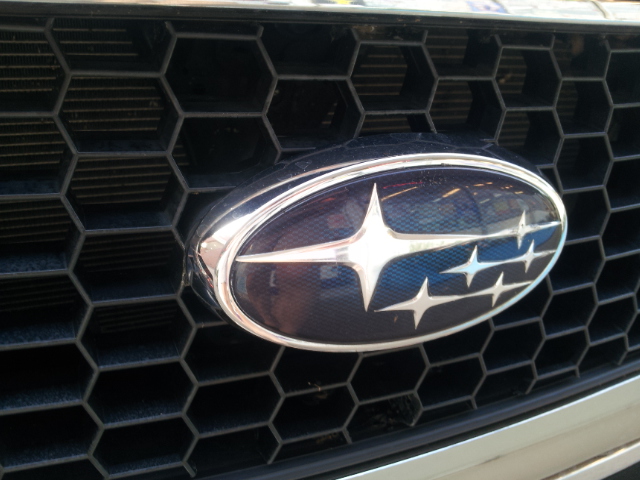 Subaru grille emblem with hexagonal pattern. Visible text 'SUPERMOTORS'