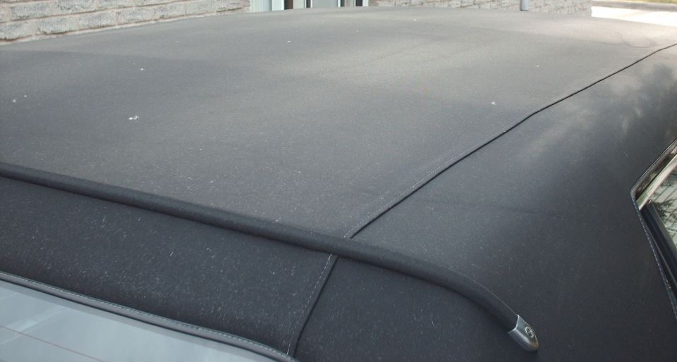Black padded vinyl roof of a sedan with seam molding and chrome trim tip