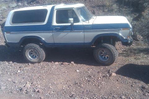 1979 Ford Bronco - A two-tone blue and white Ford Bronco is shown from a 3/4 front angle on a rocky terrain.