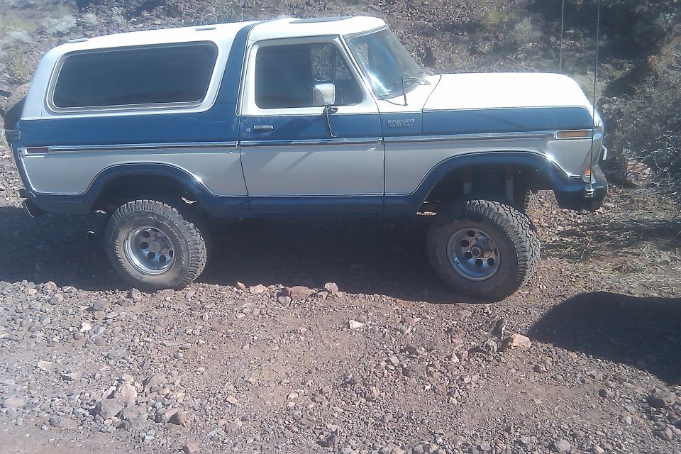 Two-tone blue and white Ford Bronco with lifted suspension and off-road tires parked on a gravelly surface