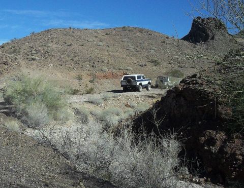 1979 Ford Bronco - Two SUVs navigate a , arid terrain under a clear blue sky.