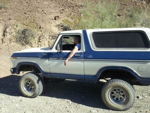 1979 Ford Bronco - A blue and white 1979 Ford Bronco is shown driving off-road.