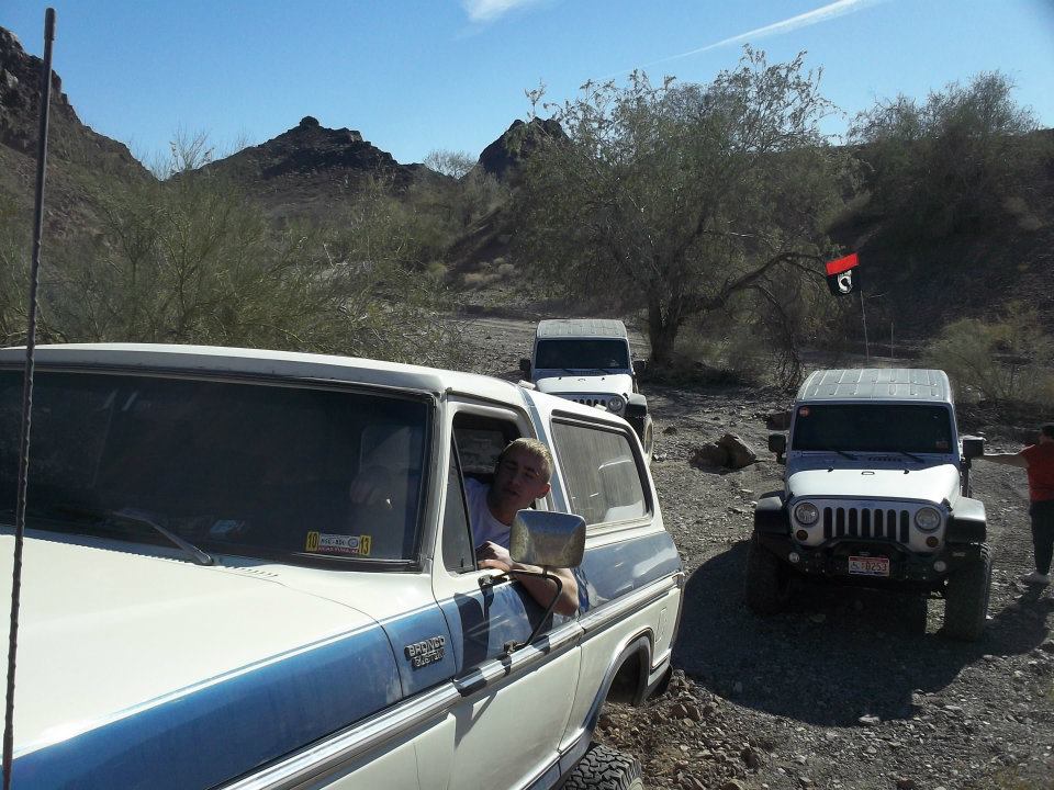 1978 Ford Bronco driving on a dirt road with two Jeeps behind it in a desert landscape