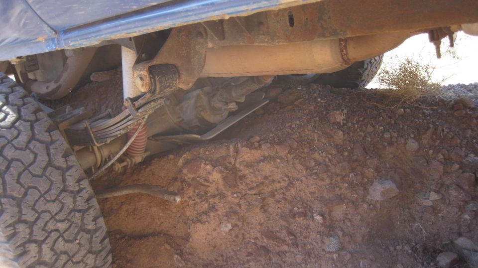 Undercarriage view of a vehicle showing leaf springs, exhaust, and tire on rough terrain