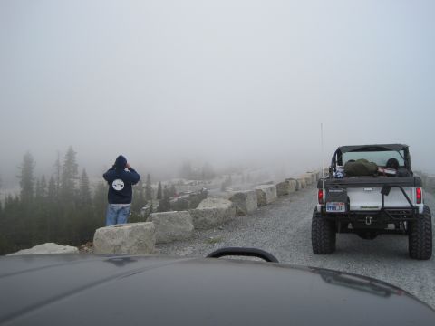 1989 Ford Bronco - A person surveys a foggy mountain vista from a gravel road, with an off-road vehicle parked nearby.