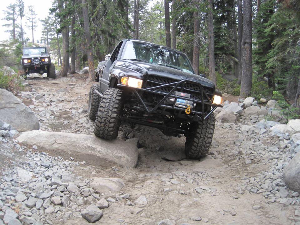 Black pickup truck with large tires navigating a rocky trail, front bumper modified with a winch