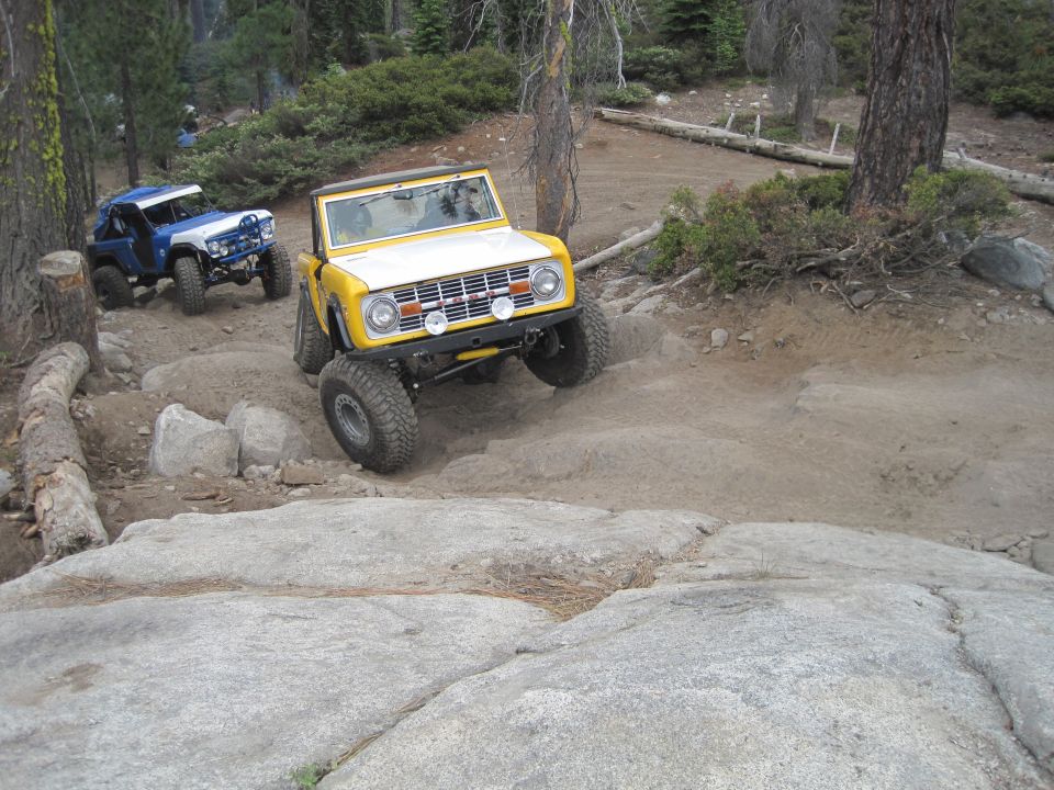 Yellow Ford Bronco and blue off-road vehicle climbing a rocky trail