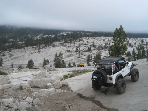 1989 Ford Bronco - A white Jeep Wrangler is parked on a road in a rocky, forested area with a yellow Jeep in the distance.
