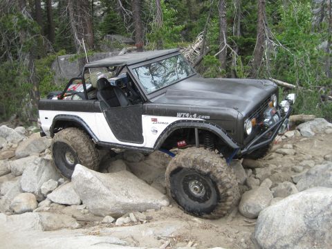1989 Ford Bronco - This modified Ford Bronco is tackling a challenging rocky trail in a wooded area.