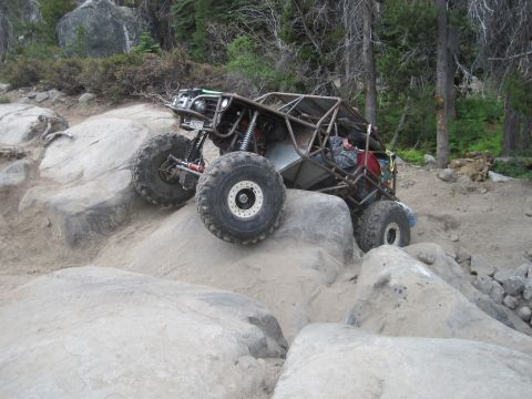 1989 Ford Bronco - A heavily modified off-road vehicle navigates a rocky terrain, its suspension and tire grip.