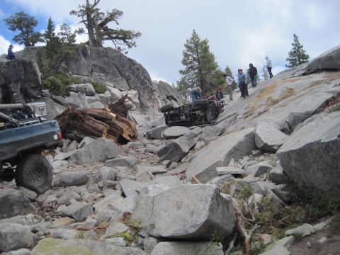 1989 Ford Bronco - An off-road vehicle has overturned on a treacherous rocky incline, with several people observing the scene.