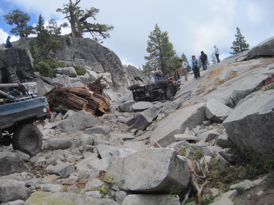 Overturned off-road vehicle on a steep, rocky slope with onlookers