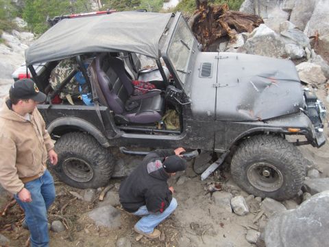 1989 Ford Bronco - A black Jeep CJ-7 is stuck on a rocky trail with two people assessing the damage.
