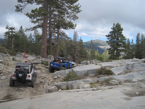 1989 Ford Bronco - A white Jeep and a blue SUV traverse a challenging rocky terrain on a mountain trail under a cloudy sky.