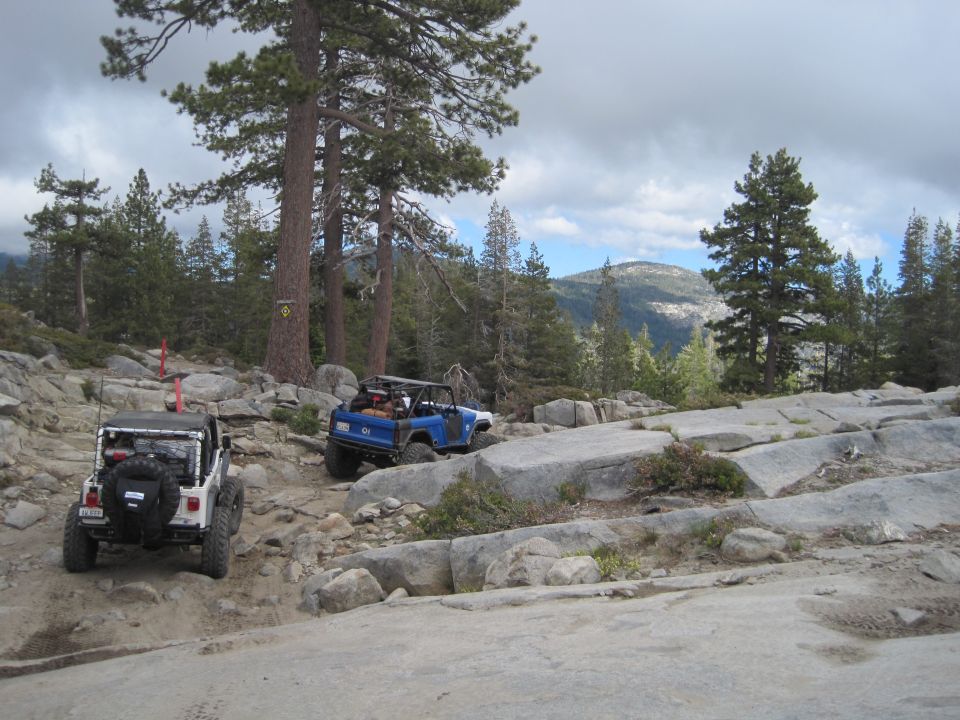 Two off-road vehicles, a white Jeep and a blue SUV, navigate a rocky mountain trail