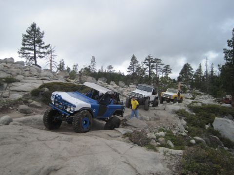 1989 Ford Bronco - Several off-road vehicles traverse a challenging rocky trail under a cloudy sky.