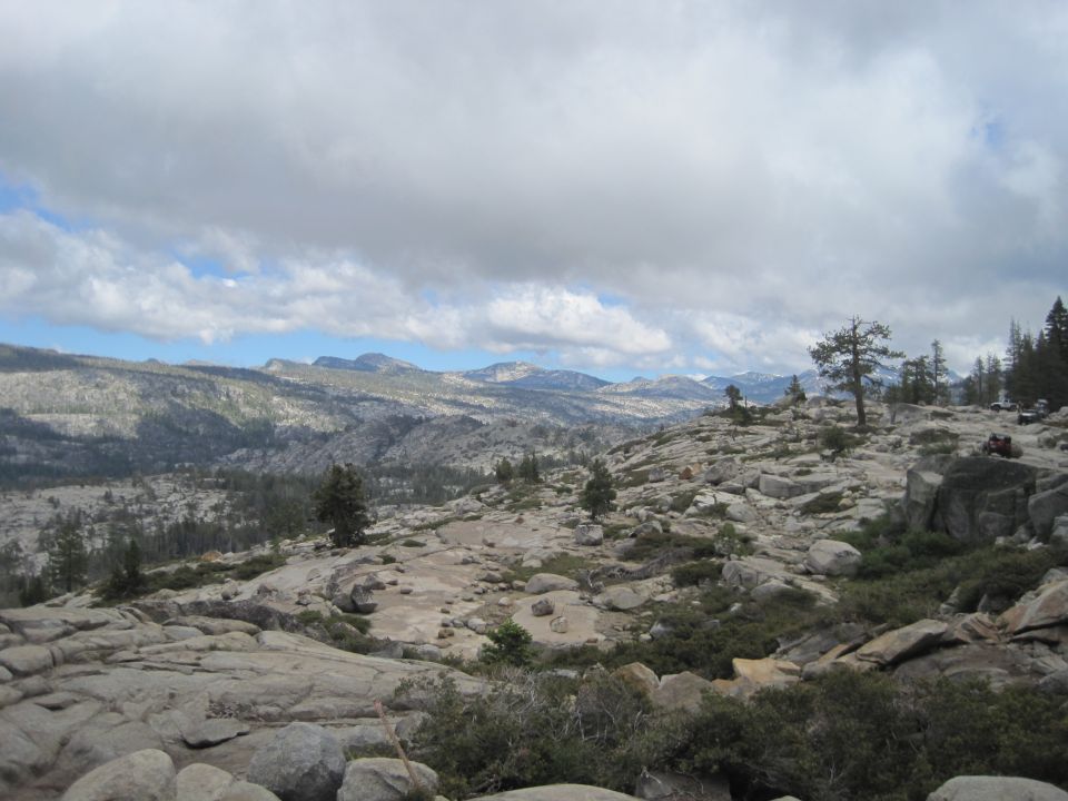Rocky mountain terrain with scattered trees and a cloudy sky