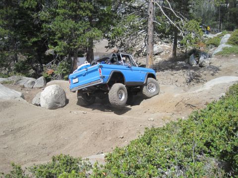1989 Ford Bronco - This lifted blue Bronco navigates a challenging off-road trail with steep inclines and rocky terrain.