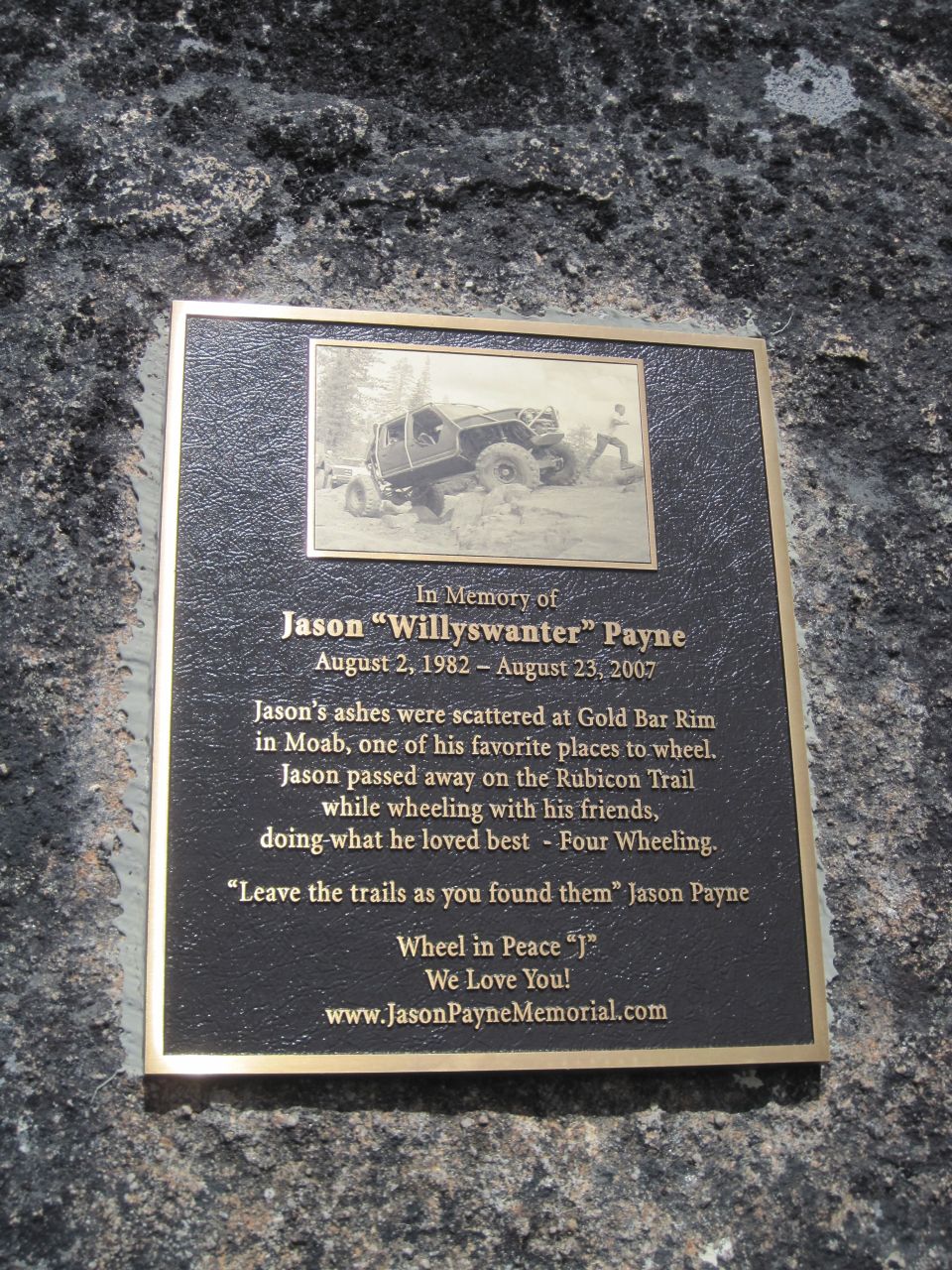 Bronze memorial plaque mounted on rock honoring Jason 'Willyswanter' Payne with a Jeep photo