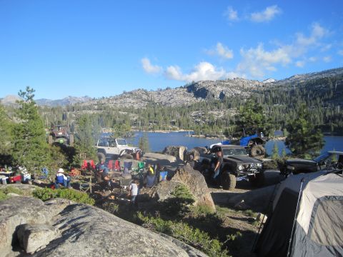 1989 Ford Bronco - A group of off-road vehicles are parked at a campsite next to a lake on a sunny day.