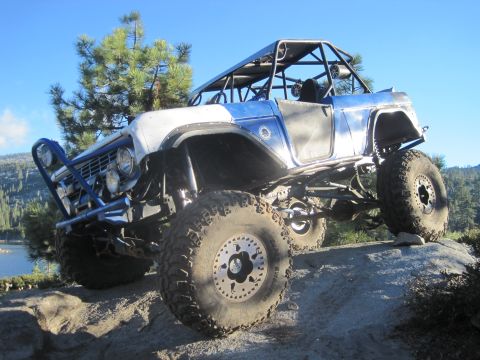 1989 Ford Bronco - This heavily modified SUV, likely a 1977 Ford Bronco, navigates rocky terrain under a clear blue sky.