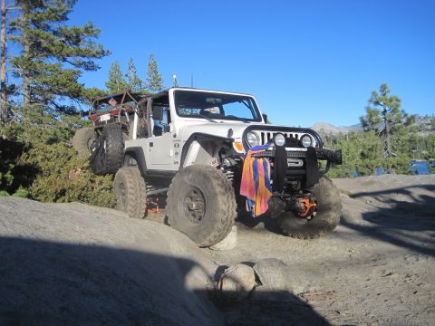 1989 Ford Bronco - Modified Jeep Wrangler tackling a challenging off-road trail with large boulders and trees.