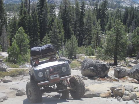 1989 Ford Bronco - A modified off-road vehicle navigates a rocky trail surrounded by trees and large boulders.