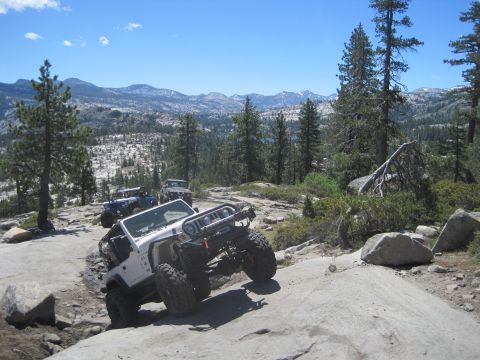 1989 Ford Bronco - Multiple off-road Jeeps climbing a challenging rocky trail in a mountainous, wooded area.