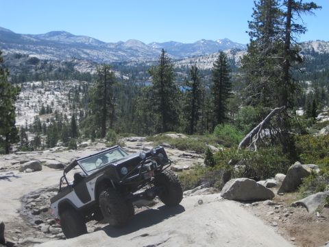 1989 Ford Bronco - Off-road vehicle navigates a challenging rocky terrain with a mountainous landscape in the background.