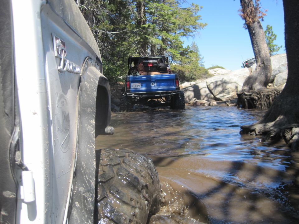 White Ford Bronco side view, driving through water with blue Bronco behind