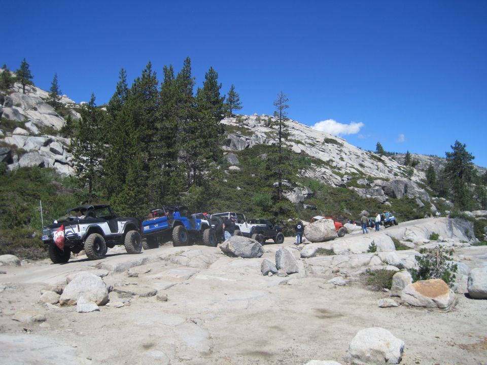 Several off-road vehicles parked on a rocky, mountainous trail under a clear blue sky