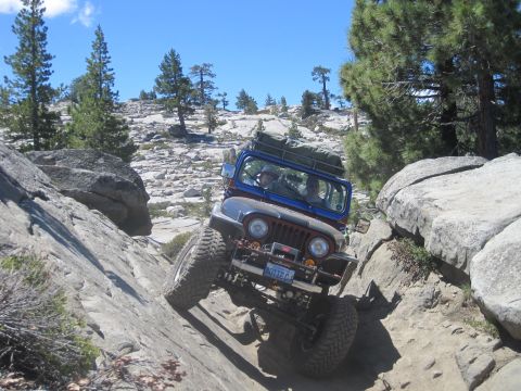 1989 Ford Bronco - Off-road Jeep CJ navigates a rocky incline under a clear blue sky.