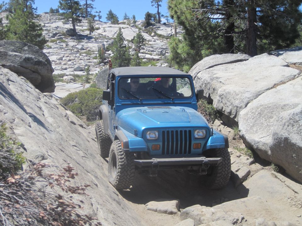 Blue Jeep Wrangler navigating a rocky trail, front view. Likely a YJ model from the early 1990s