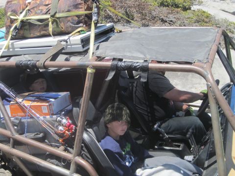 1989 Ford Bronco - Two children and a driver are inside a modified off-road vehicle loaded with fishing gear and luggage.