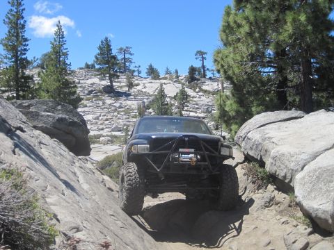 1989 Ford Bronco - Truck navigating a challenging rocky trail with large boulders and pine trees.
