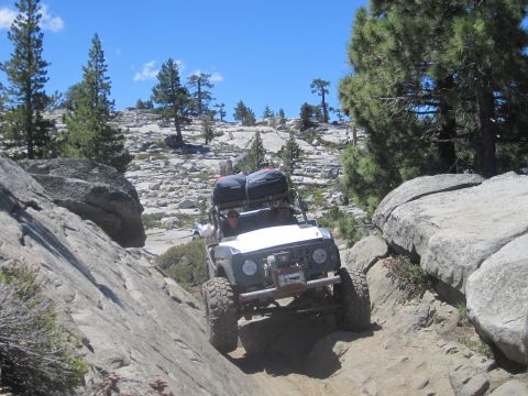 1989 Ford Bronco - A modified off-road vehicle navigates a challenging rocky path under a clear blue sky.