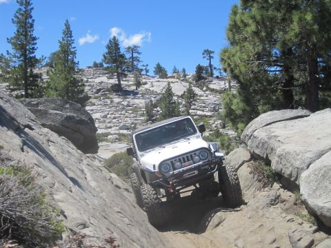 1989 Ford Bronco - A white Jeep Wrangler tackles a challenging rocky terrain on a sunny day.