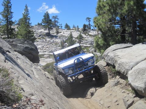 1989 Ford Bronco - This heavily modified off-road vehicle navigates a challenging rocky trail under a clear blue sky.