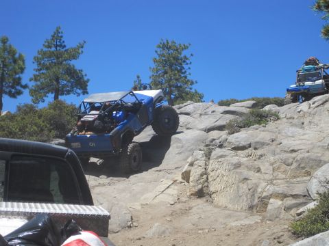 1989 Ford Bronco - Two off-road vehicles navigate a challenging rocky terrain under a clear blue sky.