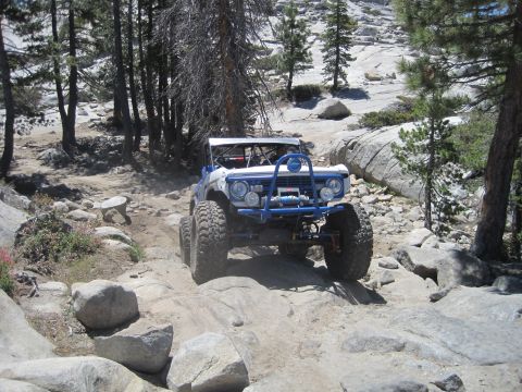1989 Ford Bronco - Modified off-road vehicle tackling a challenging rocky trail in a wooded area.