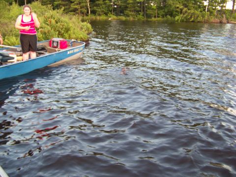 1996 Ford F-150 - A boat is on the water with a woman standing and a person swimming in the background.
