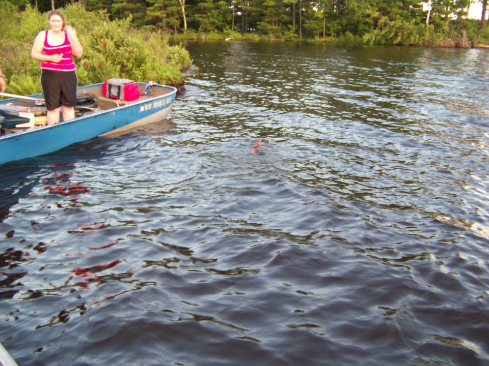 Boat on a lake with a woman standing and a person swimming