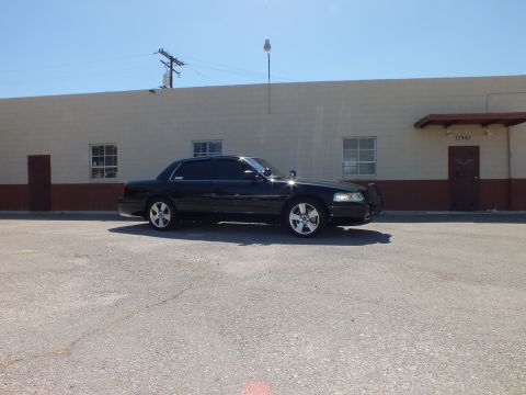 2003 Ford Crown Victoria - Side view of a lowered black sedan with tinted windows and silver multi-spoke wheels in a paved lot