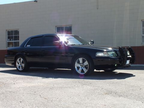 2003 Ford Crown Victoria - Front quarter of a lowered black sedan with chrome push bar and side spotlights, lens flare on glass