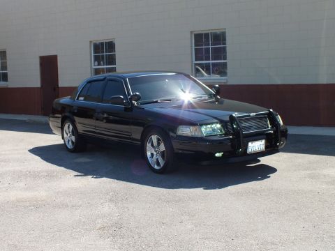 2003 Ford Crown Victoria - Black sedan front quarter showing chrome grille guard, spotlight and California front plate