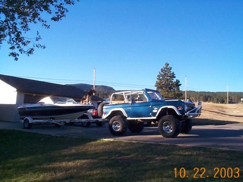 1977 Ford Bronco - A blue Ford Bronco tows a boat on a trailer under a clear blue sky.