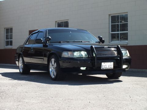 2003 Ford Crown Victoria - Front three-quarter of a black sedan; front plate reads EVIL VIC above a chrome push bar.