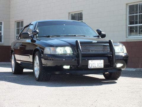 2003 Ford Crown Victoria - Low front three-quarter of a black sedan; Ford-badged plate frame and EVIL VIC tag visible.