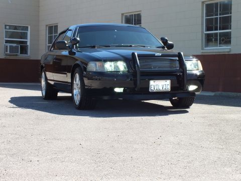 2003 Ford Crown Victoria - Front-right view of a black sedan with EVIL VIC plate, billet grille and bright chrome rims.
