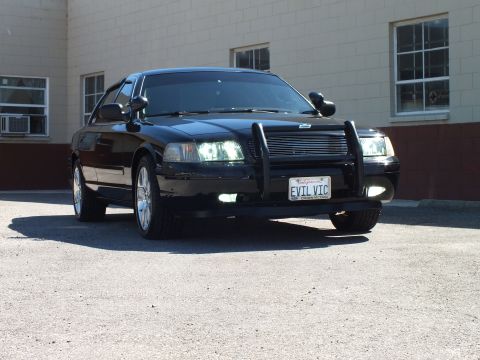 2003 Ford Crown Victoria - Front three-quarter of a black sedan; California plate reads EVIL VIC behind a push bar.